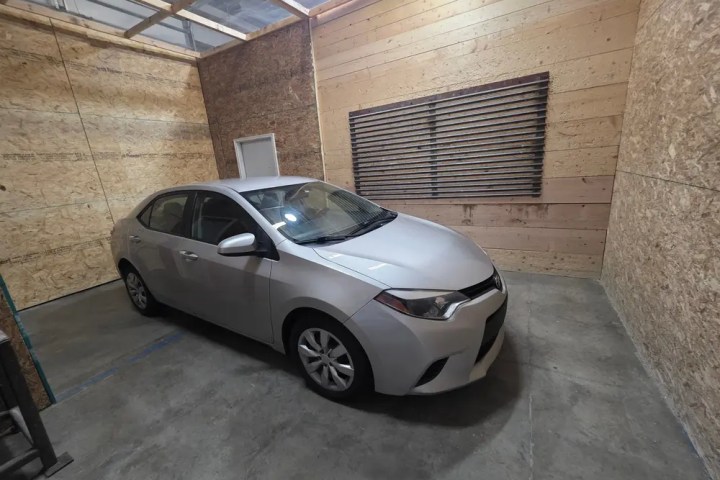 Silver sedan parked in a wooden panel garage with a vented window.